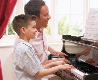 Father and son sitting together at a grand piano, both smiling