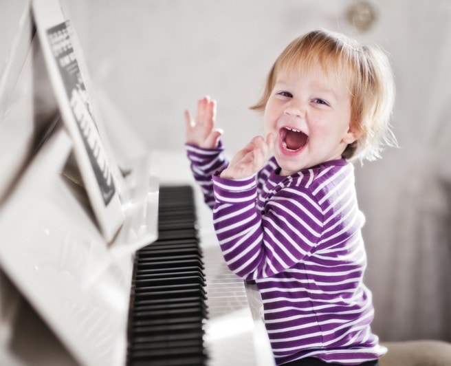 Joyful young child clapping hands at a white piano