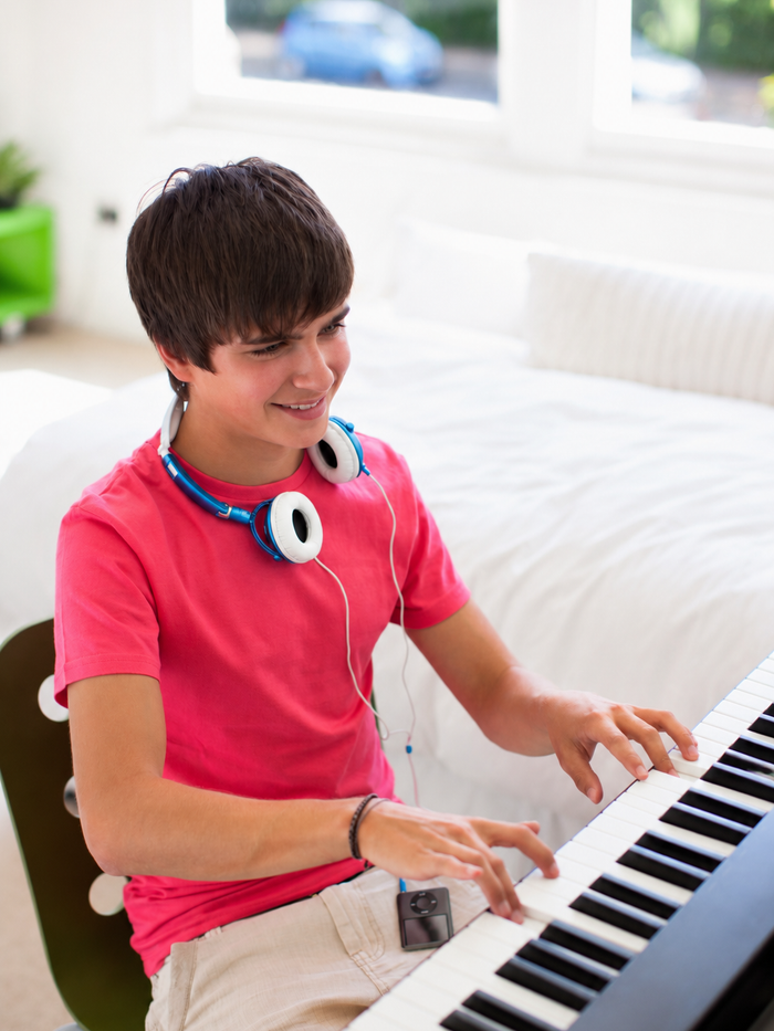 Smiling teenager with headphones playing keyboard piano